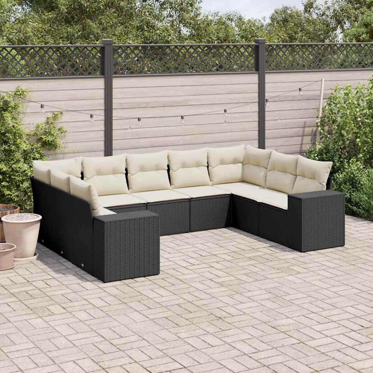 Schwarzes Korbsessel-Ecksofa im Freien mit weißen Kissen auf einer Ziegelterrasse, mit Pflanzen.