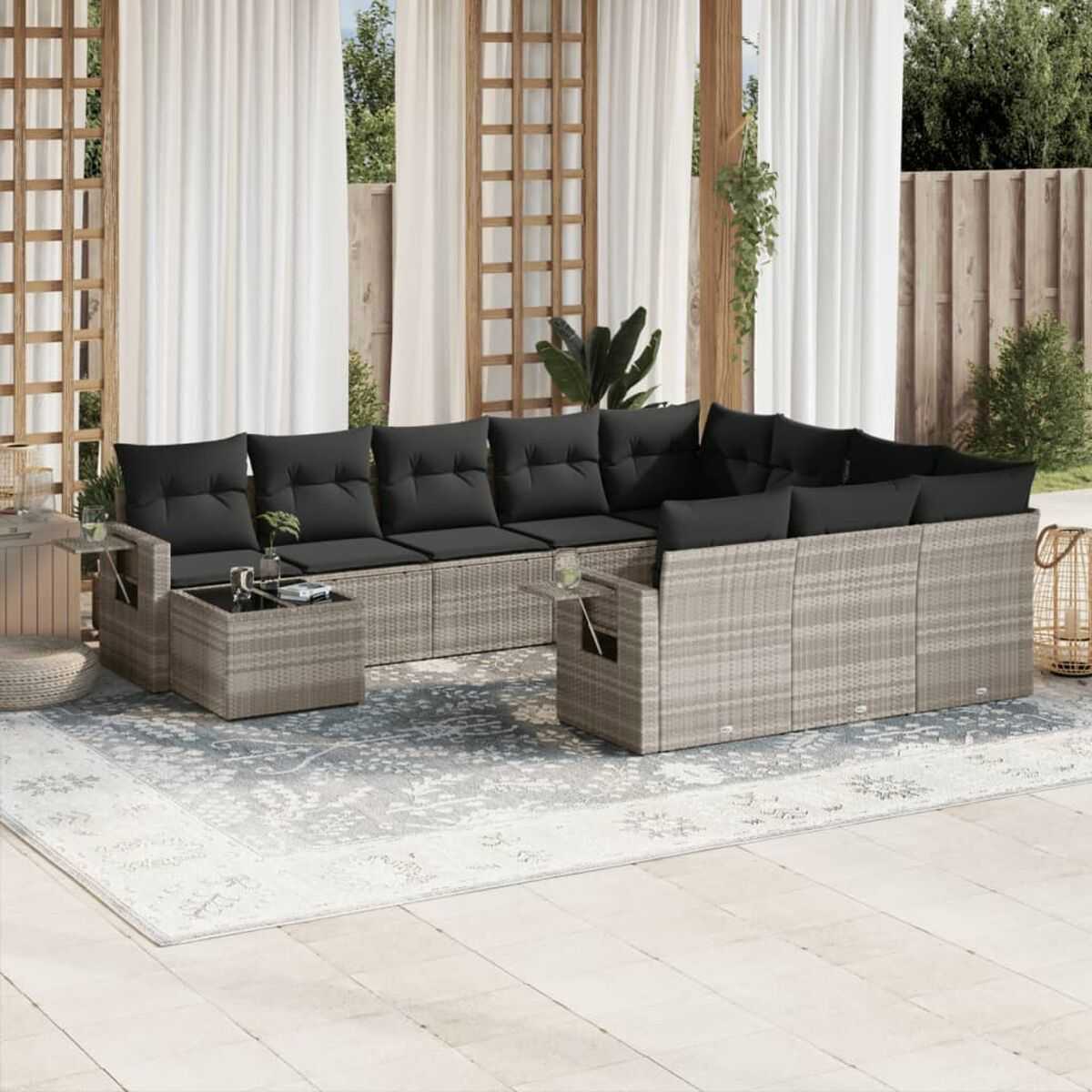 Outdoor-Flecht-Ecksofa mit grauen Kissen, kleinen Tischen und Teppich. Vorhänge und Pflanzen im Hintergrund.