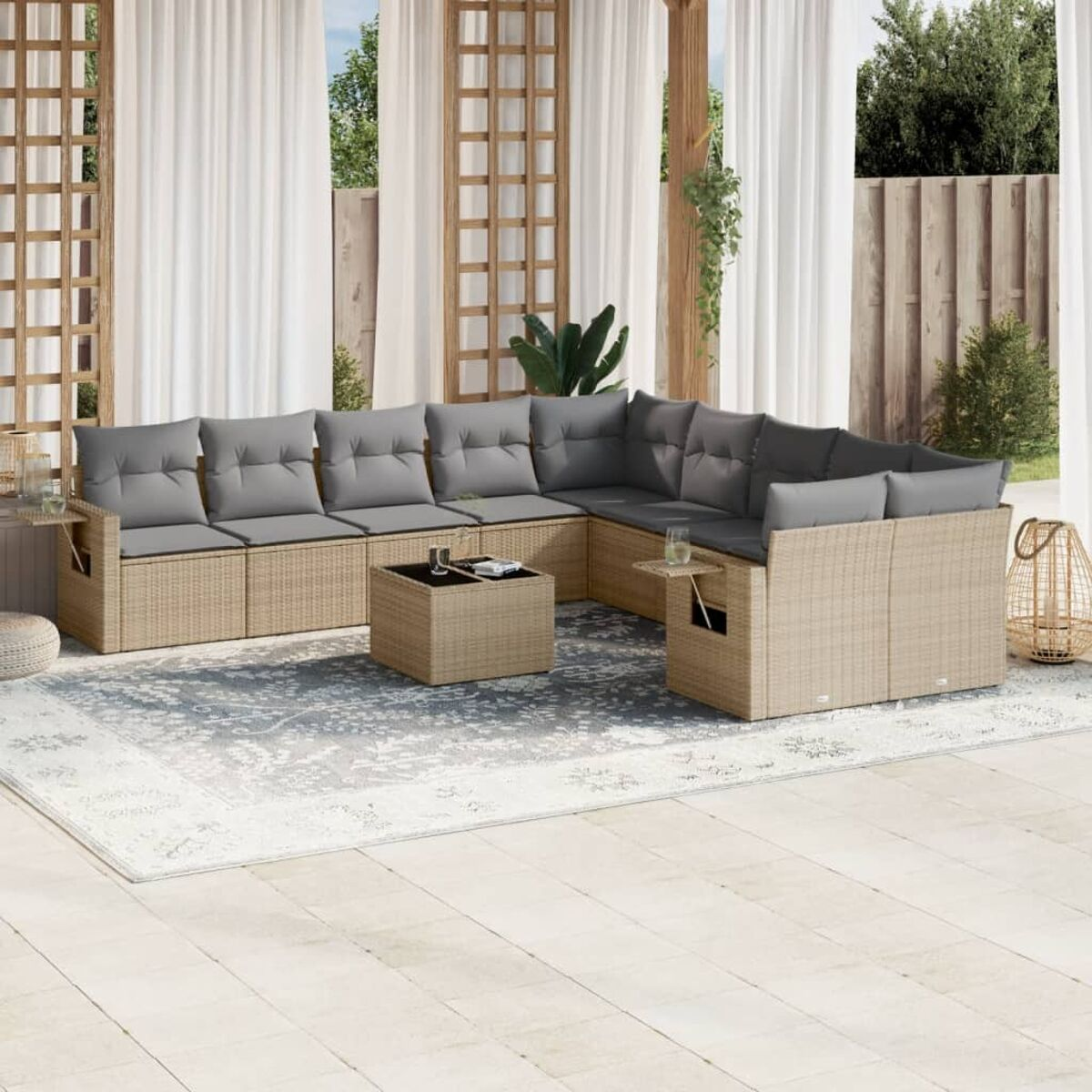 Rattan-Ecksofa mit grauen Kissen, Couchtisch und Beistelltischen. Weiße Vorhänge und Holzstruktur.