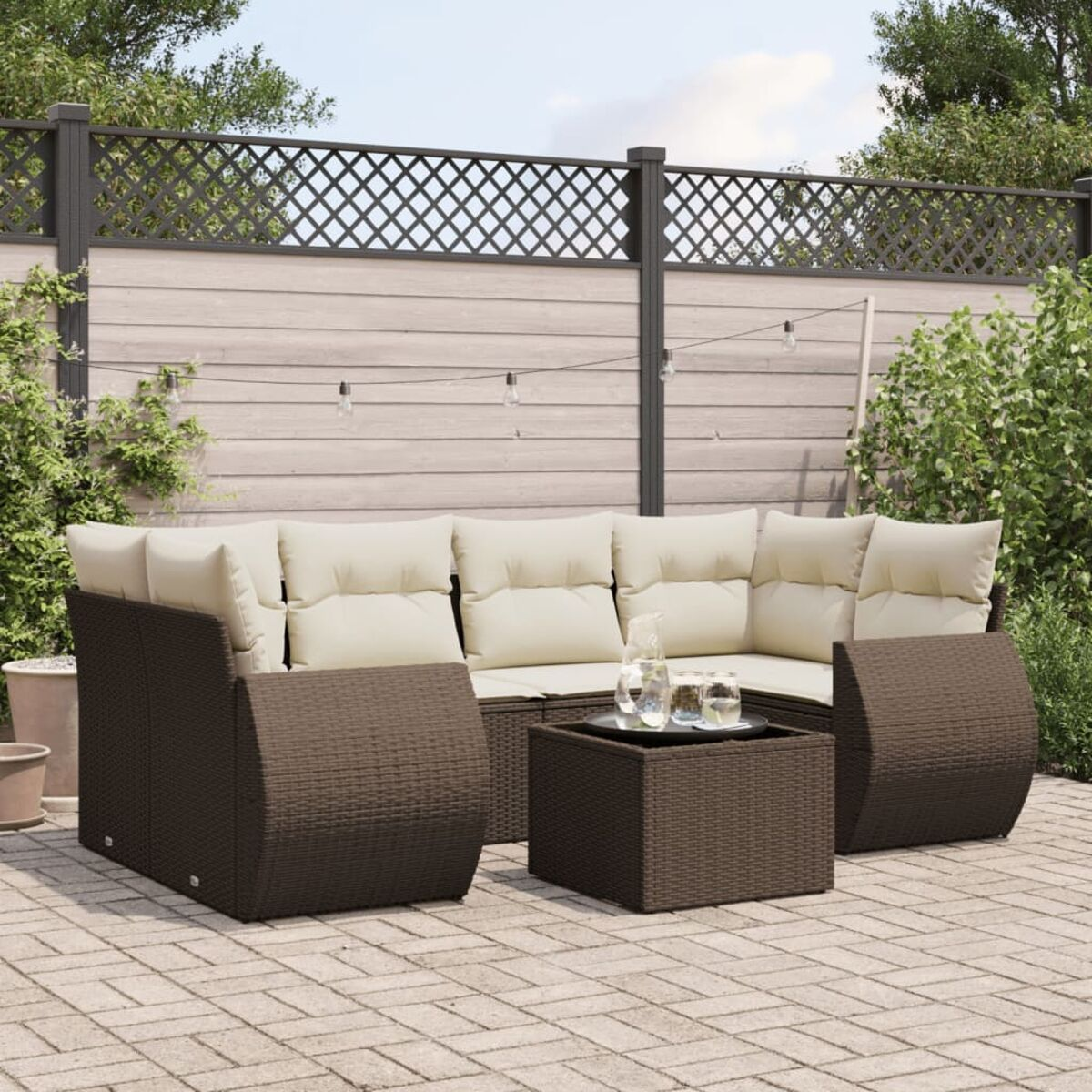 Set divano in rattan marrone scuro con cuscini beige e tavolino, su un patio in pietra.