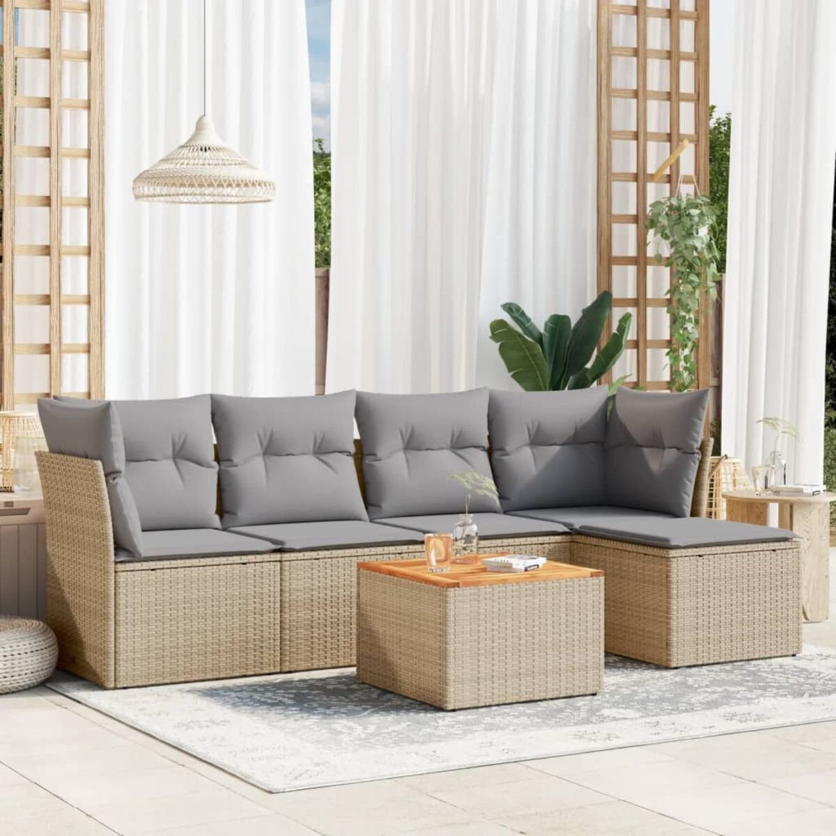 Beiges Rattan-Sofaset mit grauen Kissen und einem Holztisch auf einem gemusterten Teppich, in einem Raum.