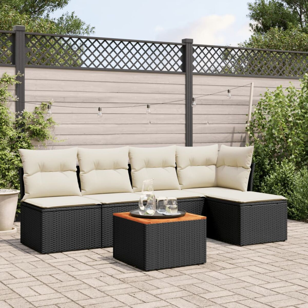 Schwarzes Outdoor-Ecksofa aus Korbgeflecht mit cremefarbenen Kissen und einem Tisch mit Getränken auf einer Ziegelterrasse.