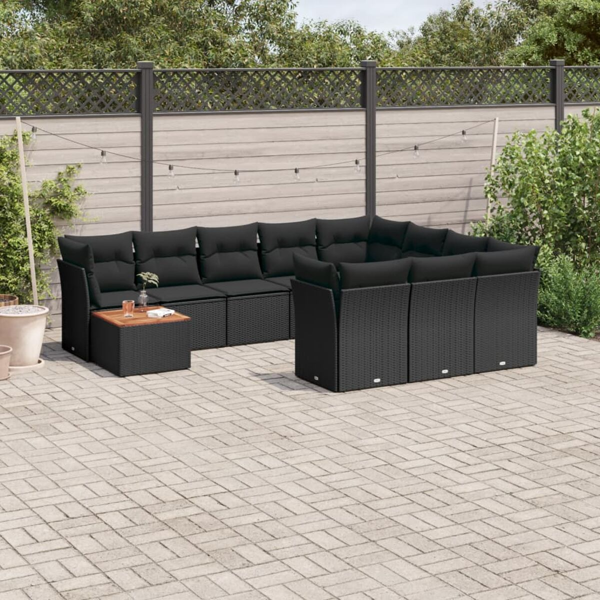 Schwarzes Ecksofa aus Rattan mit schwarzen Kissen, kleiner Tisch auf einer Backstein-Terrasse.