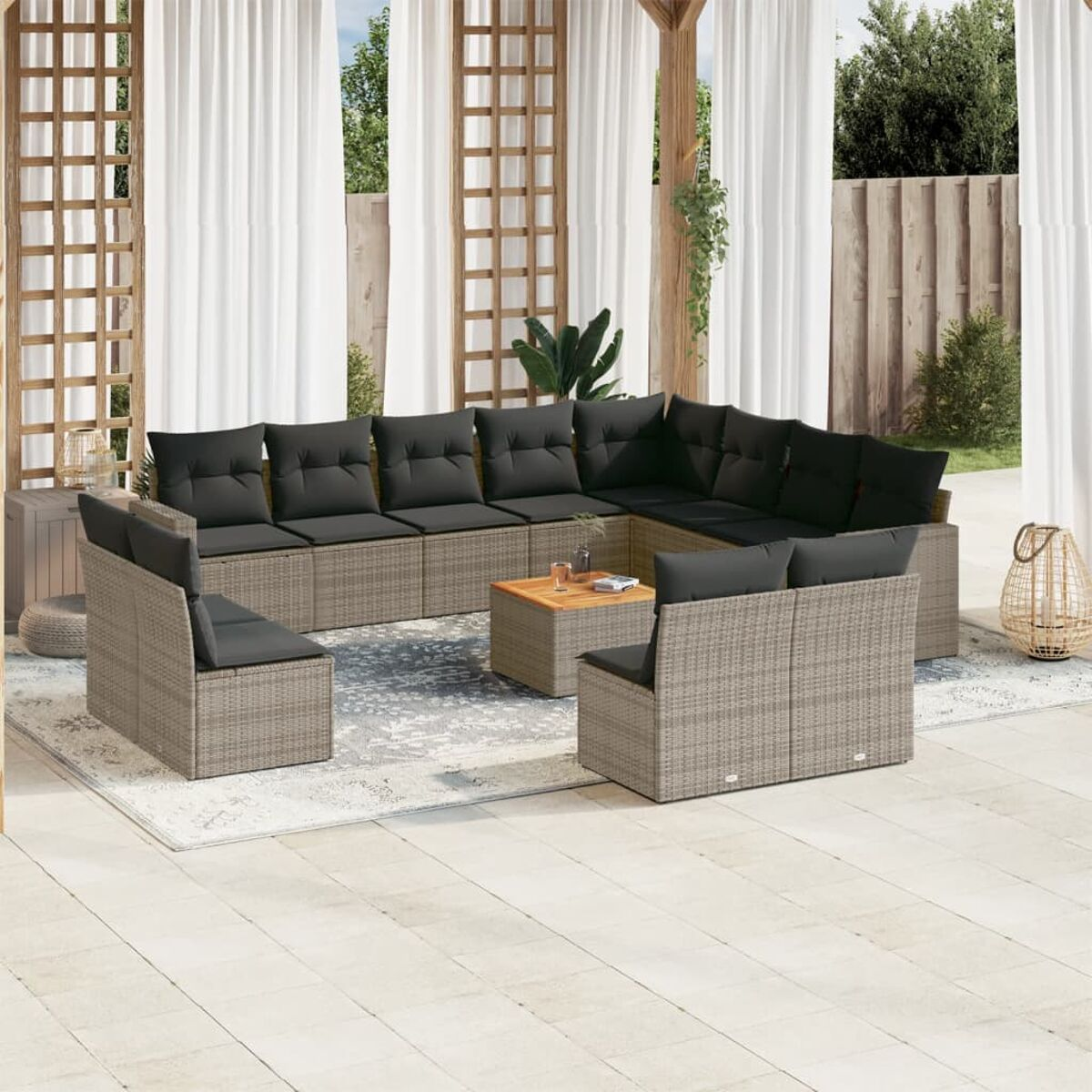 Graues Korbmöbel-Ecksofa mit grauen Kissen und einem Holztisch auf einer Terrasse. Pflanzen im Hintergrund.