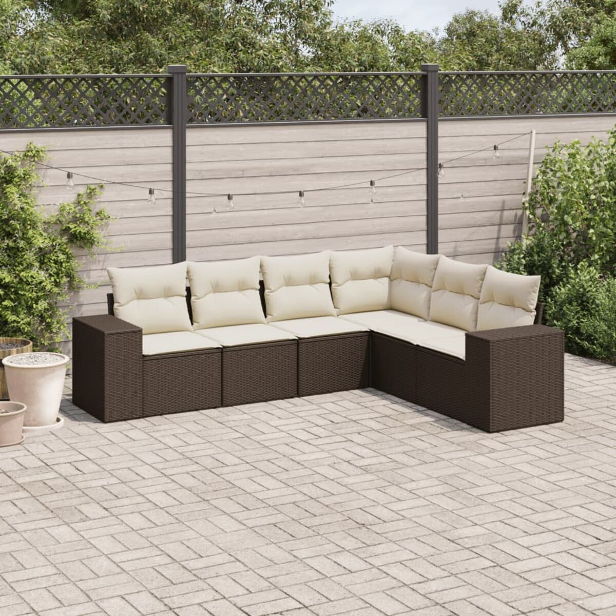 Divano angolare esterno marrone con cuscini color crema su un patio pavimentato con recinzione.
