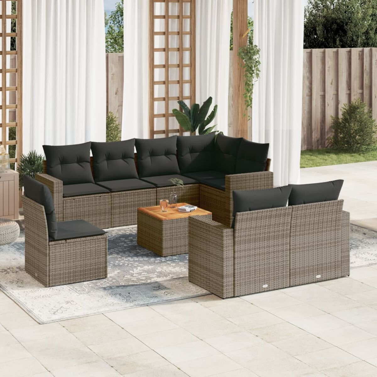 Sofa, Stühle und Tisch aus Korbgeflecht mit grauen Kissen auf gemustertem Teppich, Vorhänge.