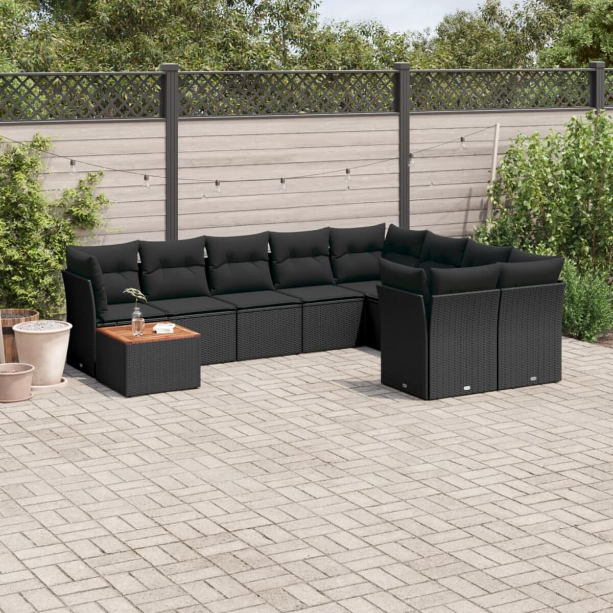 Outdoor-Ecksofa auf einer Ziegelterrasse. Das Sofa ist schwarz und hat schwarze Kissen.