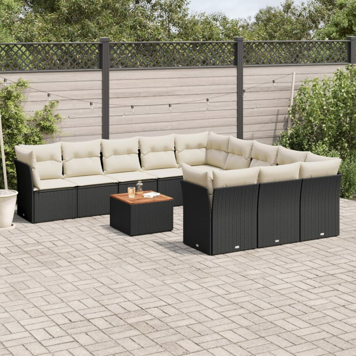 Schwarzes Outdoor-Ecksofa aus Korbgeflecht mit Kissen und Tisch. Ziegel-Patio und grüner Hintergrund.