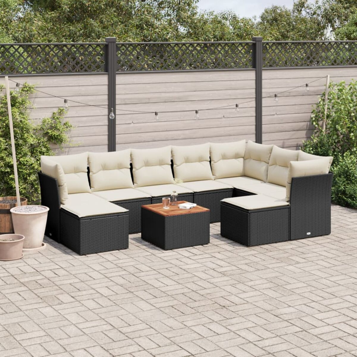 Schwarzes Ecksofa aus Korbgeflecht mit cremefarbenen Kissen und einem Holztisch auf einer Ziegelterrasse.