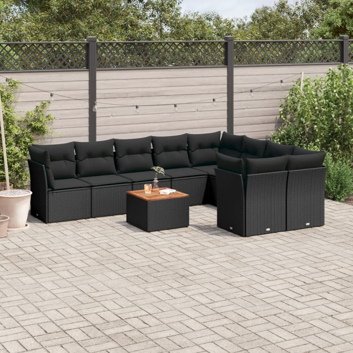 Ein schwarzes Outdoor-Möbelset aus Korbgeflecht mit Sofa, Ecksofa und Couchtisch auf einer Ziegelterrasse.