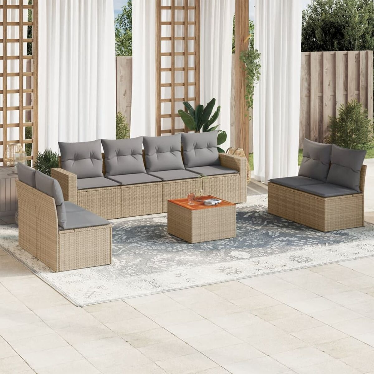 Outdoor-Ecksofa aus Rattan mit grauen Kissen und kleinem Tisch. Weißer Teppich und Vorhänge im Hintergrund.