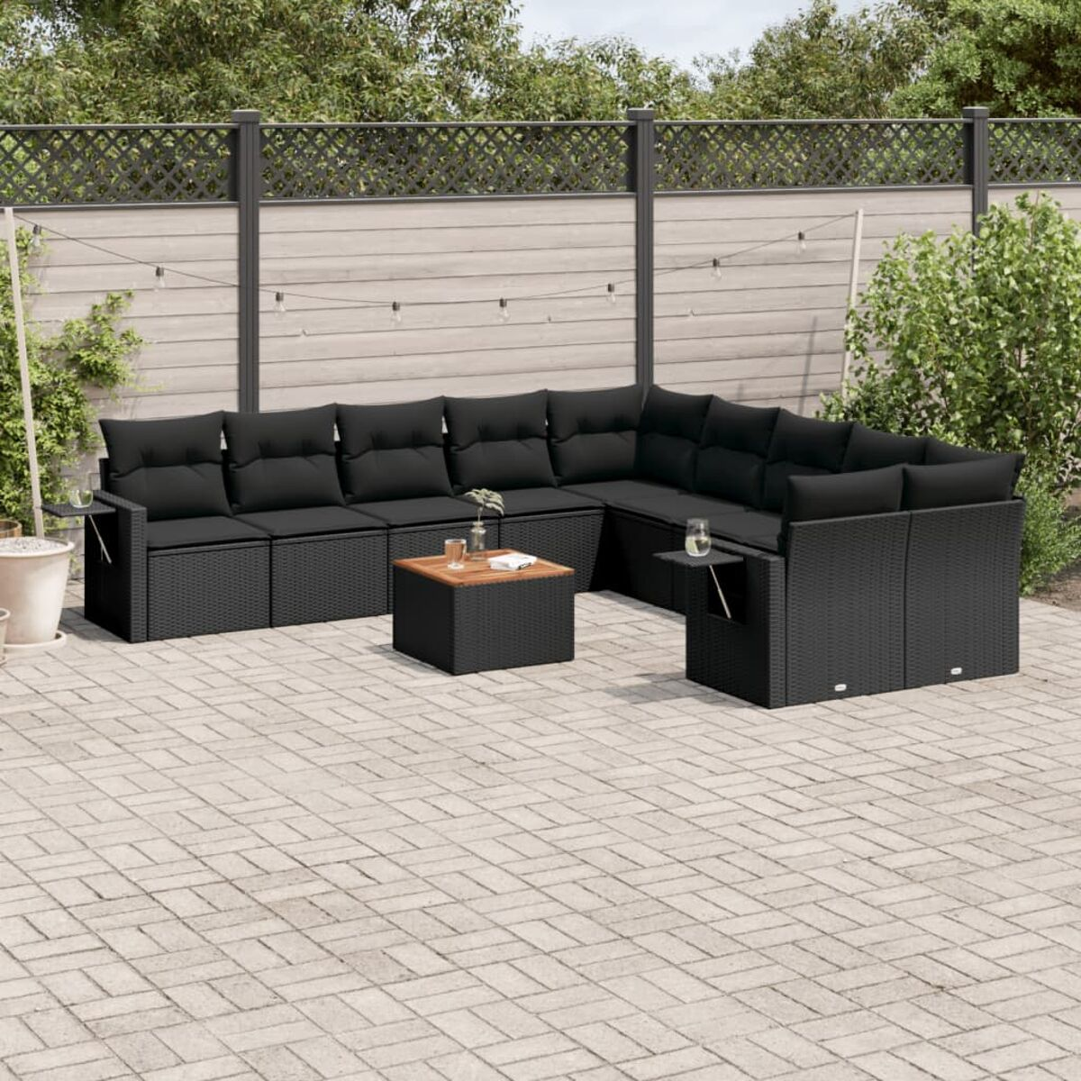 Ein schwarzes Ecksofa aus Korbgeflecht mit schwarzen Kissen und einem Couchtisch auf einer Ziegelterrasse.