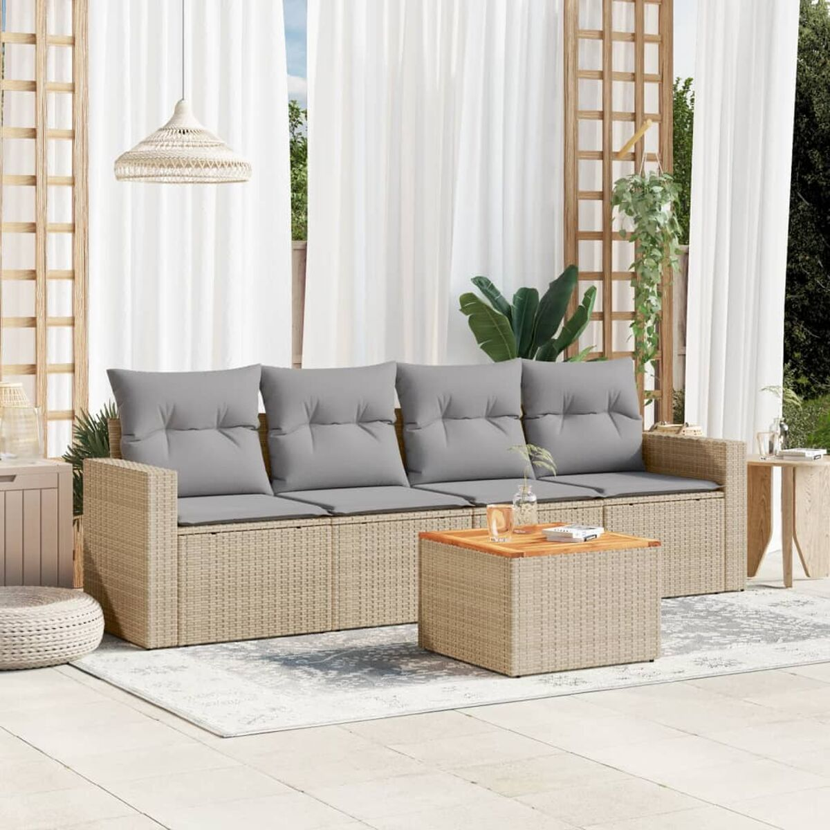 Beiges Korbmöbel-Sofa mit grauen Kissen auf einem Teppich, ein quadratischer Tisch davor. Vorhänge im Hintergrund.