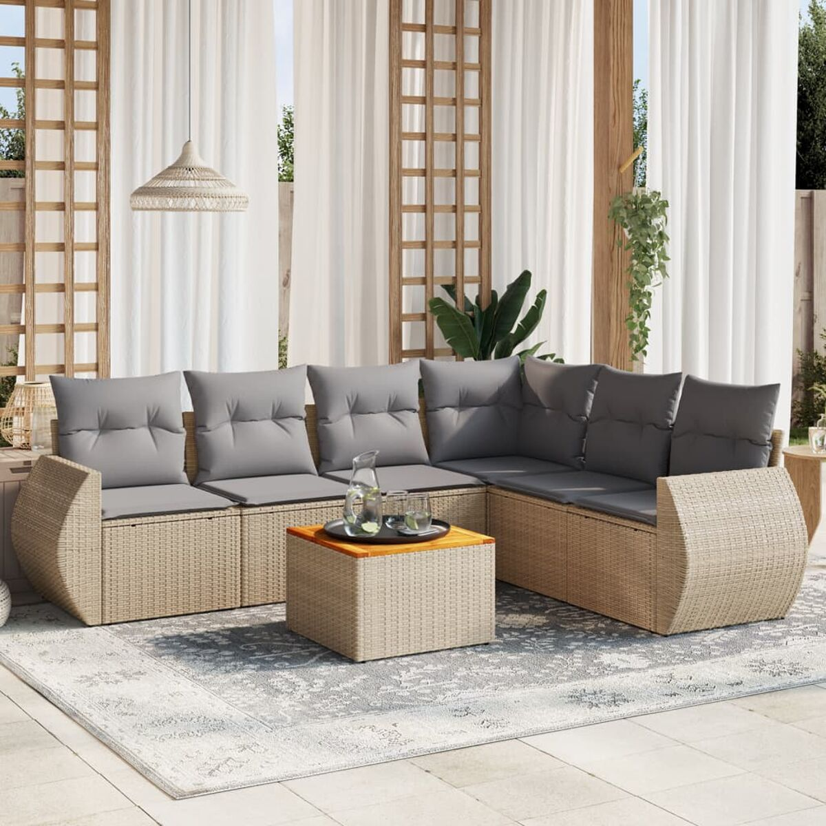 Rattan-Sofagarnitur mit grauen Kissen und einem Holztisch, auf einem gemusterten Teppich, mit Vorhängen im Hintergrund.