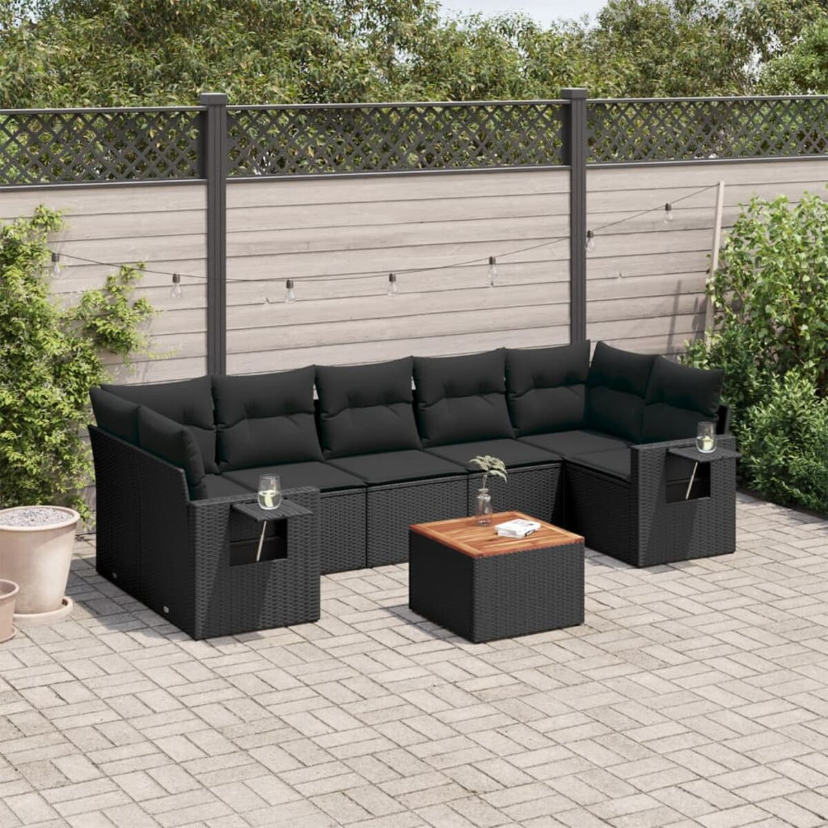 Schwarzes Rattan-Ecksofa mit schwarzen Kissen, kleinem Tisch und Gläsern in einem Hinterhof.