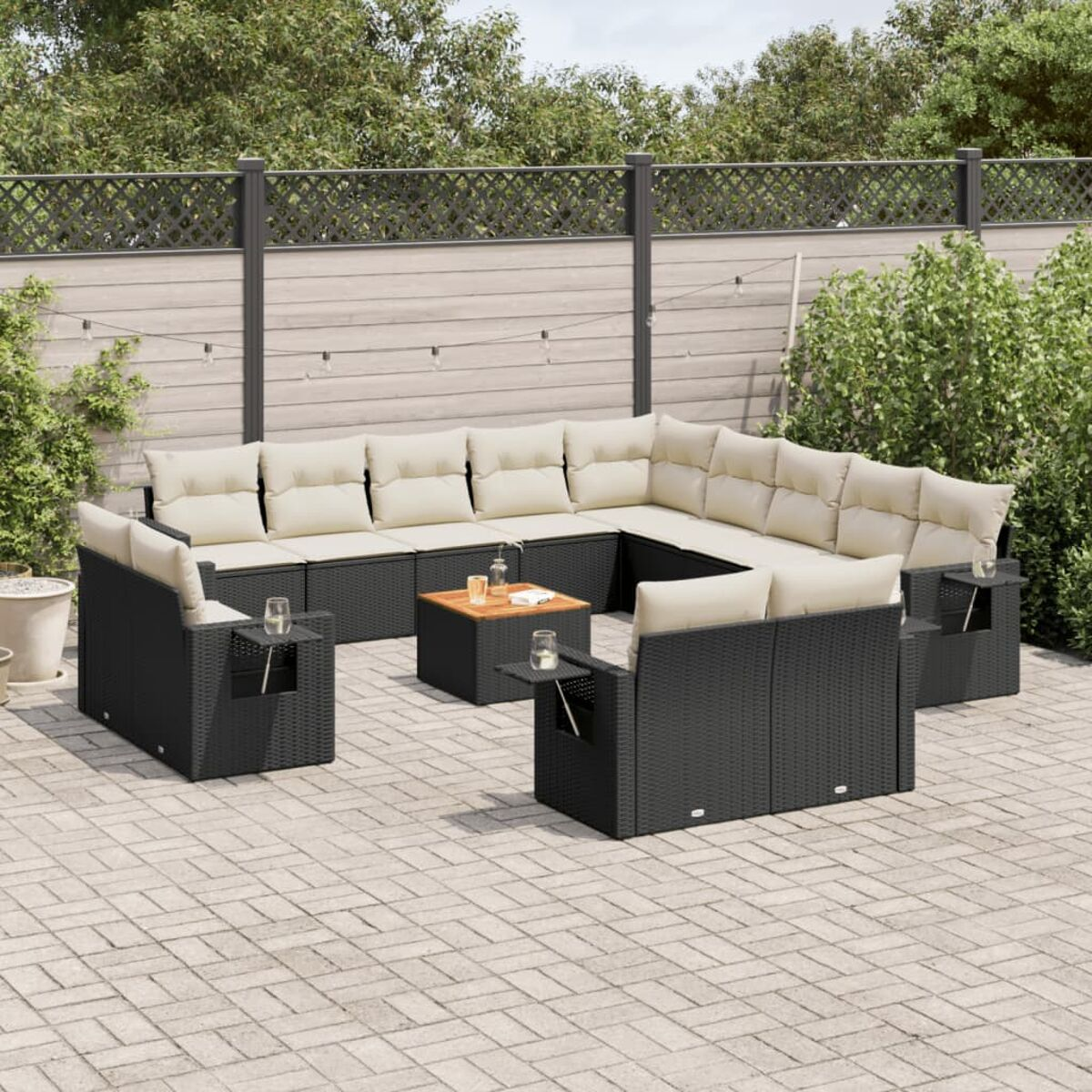 Schwarzes Wicker-Outdoor-Ecksofa mit beigen Kissen, Couchtisch und Beistelltischen. Gepflasterte Terrasse.