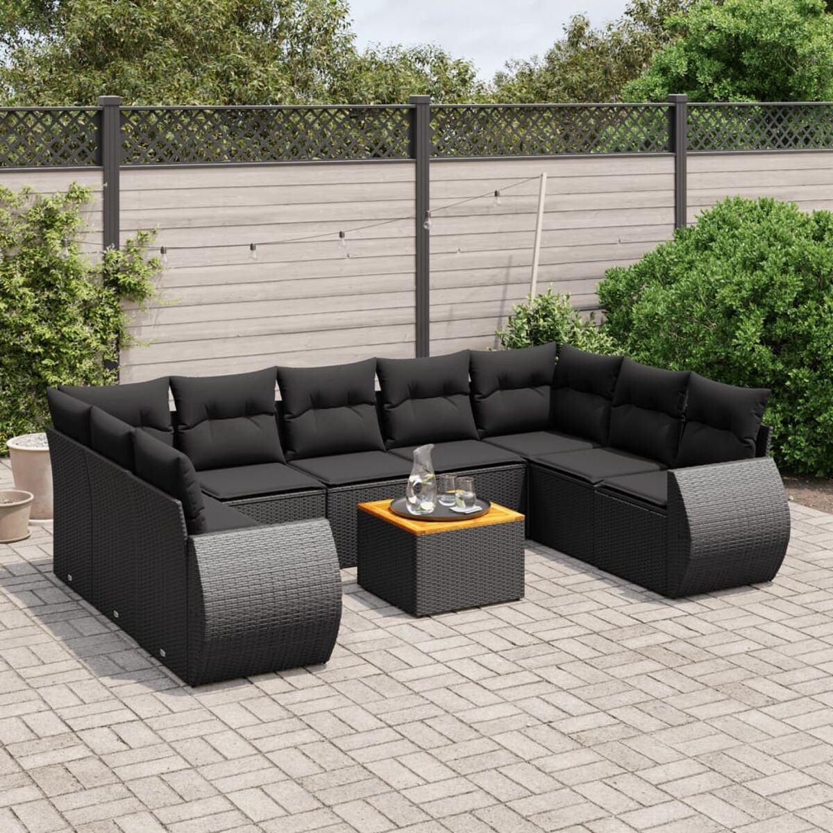 Schwarzes Korbmöbel-Set mit schwarzen Kissen, Tisch auf Terrasse. Garten im Hintergrund.