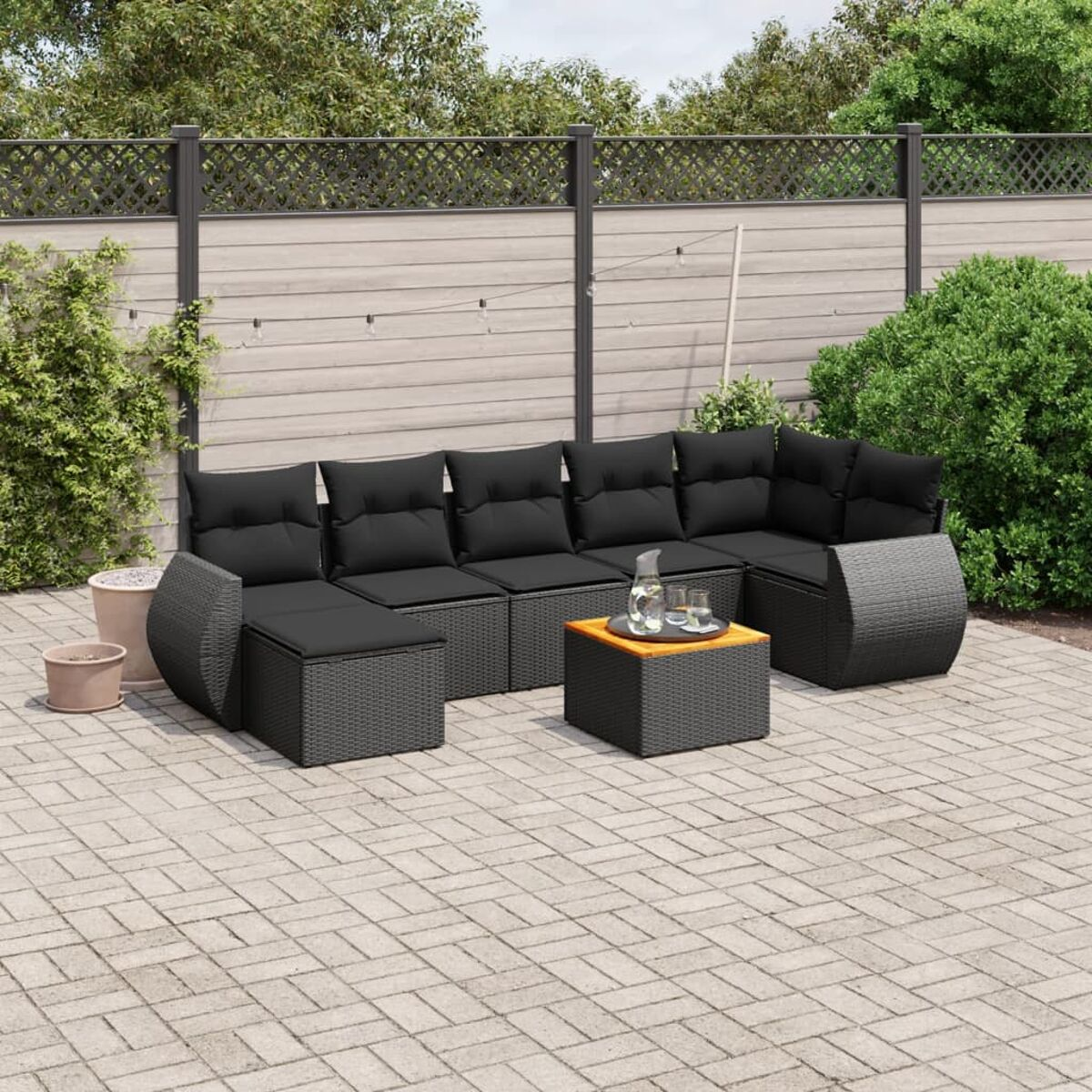 Schwarzes Ecksofa aus Korbgeflecht mit Couchtisch auf einer Backstein-Terrasse. Outdoor-Setting mit Gläsern.