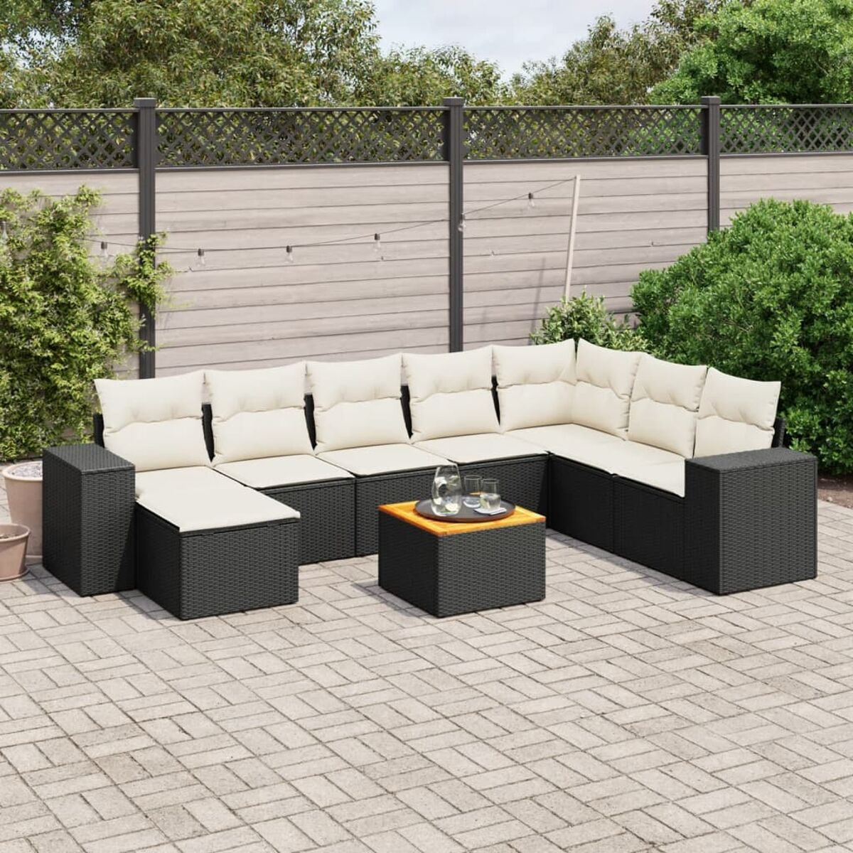 Ein Terrassen-Set mit braunem Korbgeflecht und cremefarbenen Kissen. Enthält ein großes Ecksofa und einen Tisch auf einer Ziegelterrasse.