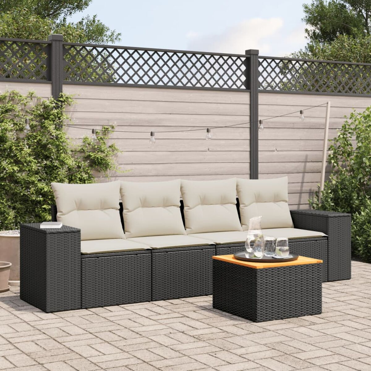 Dunkelgraues Rattan-Sofa mit beigen Kissen, einem Couchtisch mit Gläsern und einer Kanne. Eine Ziegelterrasse und ein Zaun.