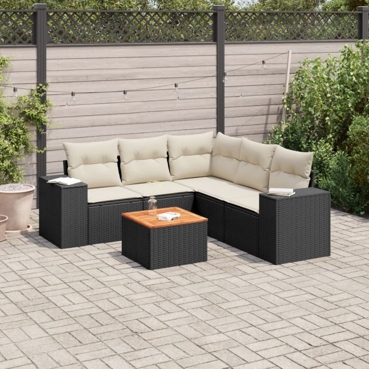 Schwarzes Rattan-Outdoor-Sofa-Set mit Couchtisch. Auf einer Steinterrasse mit Grün.