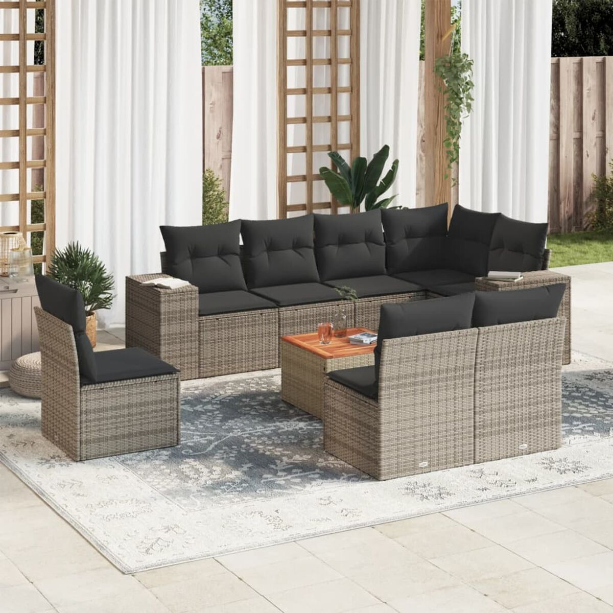 Geflochtenes Outdoor-Sofaset mit Kissen, Couchtisch mit Holzplatte, auf einem gemusterten Teppich.