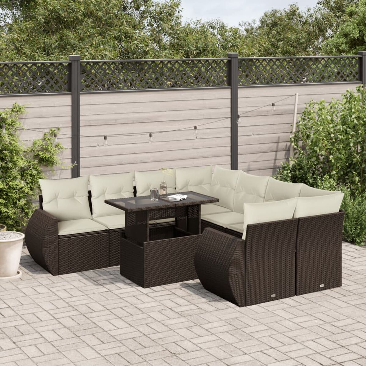 Braunes Ecksofa aus Korbgeflecht mit Tisch, auf Steinpflaster, mit Zaun und Pflanzen.