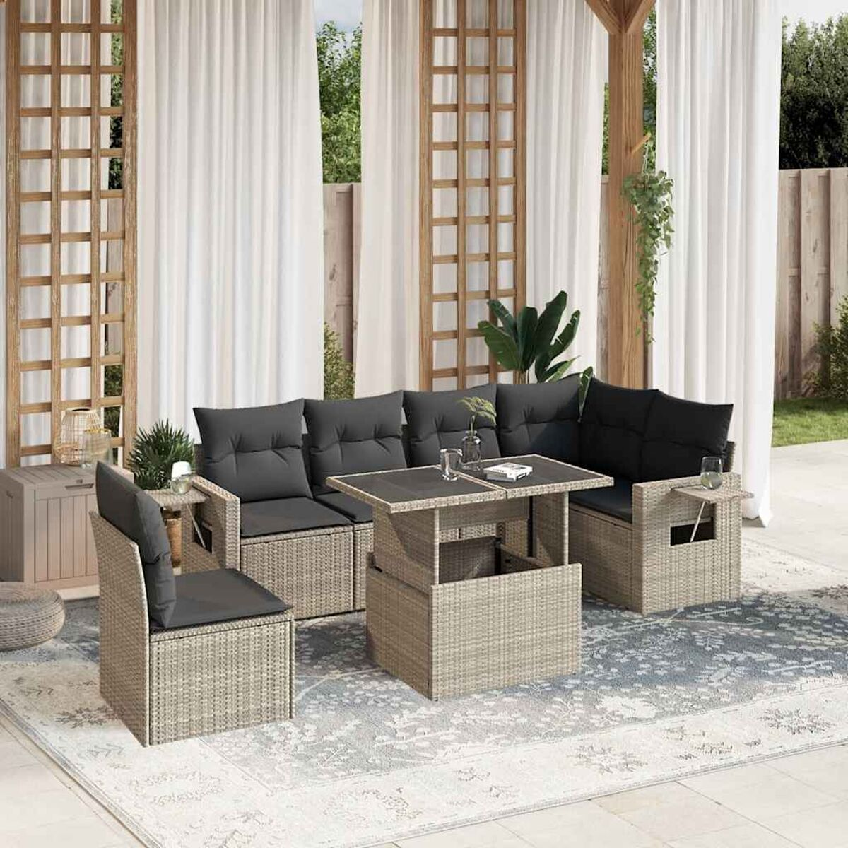 Ein Rattan-Terrassenset mit Tisch, Sofa und Stuhl. Schwarze Kissen auf den Möbeln. Weiße Vorhänge im Hintergrund.