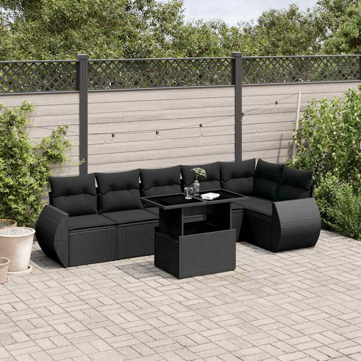 Schwarzes Rattan-Outdoor-Sofaset mit Tisch auf einer Ziegelterrasse. Grün und ein Zaun im Hintergrund.