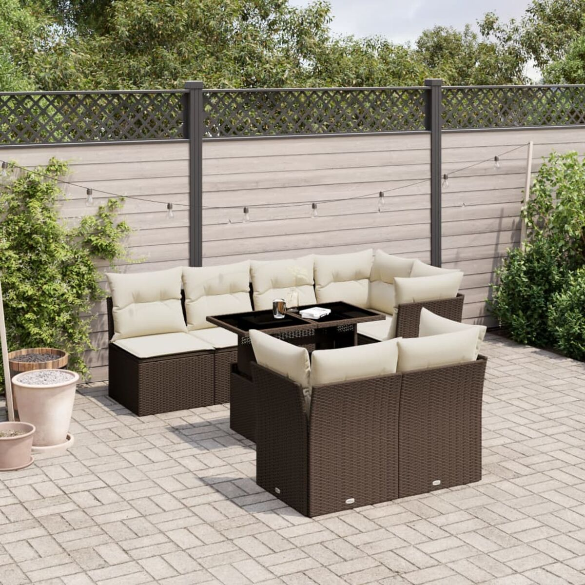 Braunes Outdoor-Sofa mit beigen Kissen, Tisch, auf Ziegelpflaster und Zaun.