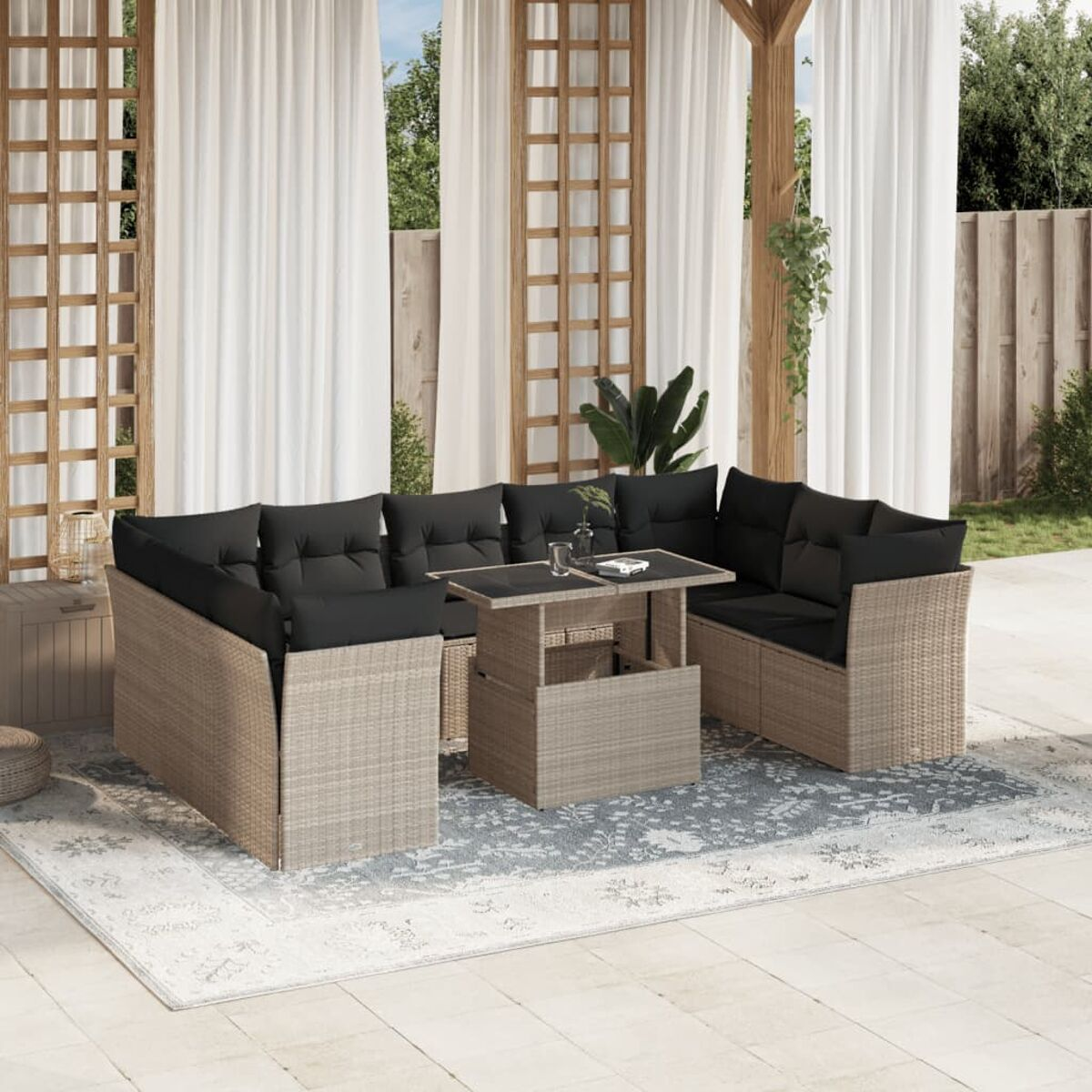 Beiges Ecksofa-Set aus Rattan für den Außenbereich mit schwarzen Kissen, einem Couchtisch und einem Teppich. Vorhänge im Hintergrund.