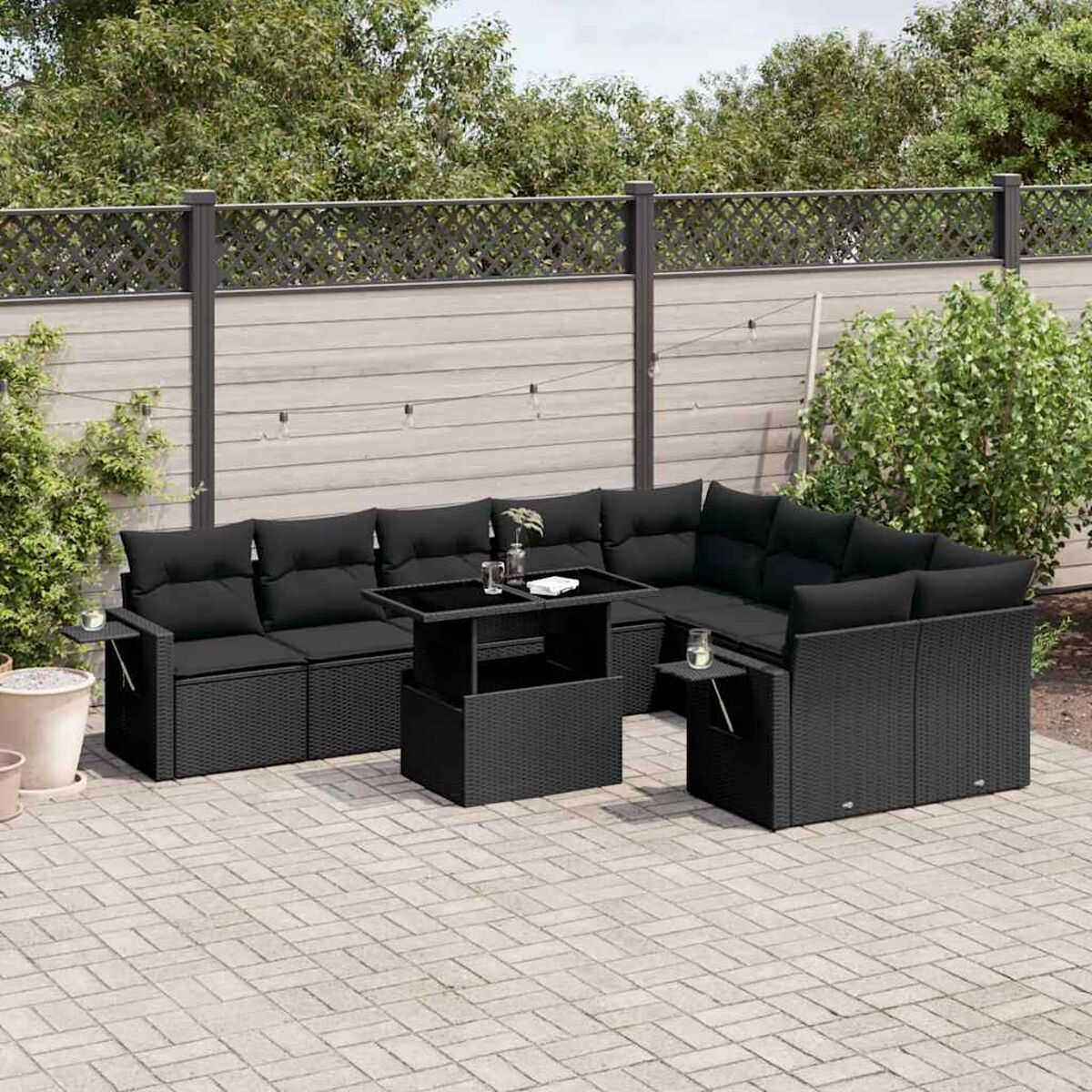 Schwarzes Outdoor-Geflecht-Ecksofa-Set mit Tisch auf einer Terrasse, mit Pflanzen im Hintergrund.