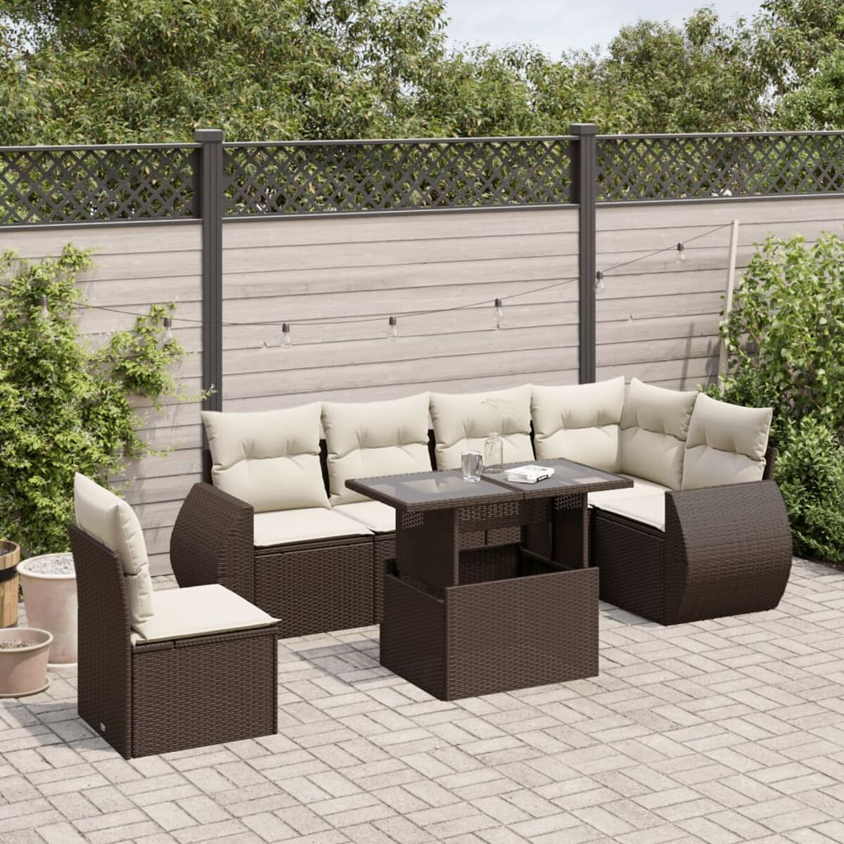 Braunes Outdoor-Korbmöbel-Set: Sofa, Tisch und Stuhl auf einer gepflasterten Terrasse, Zaun im Hintergrund.