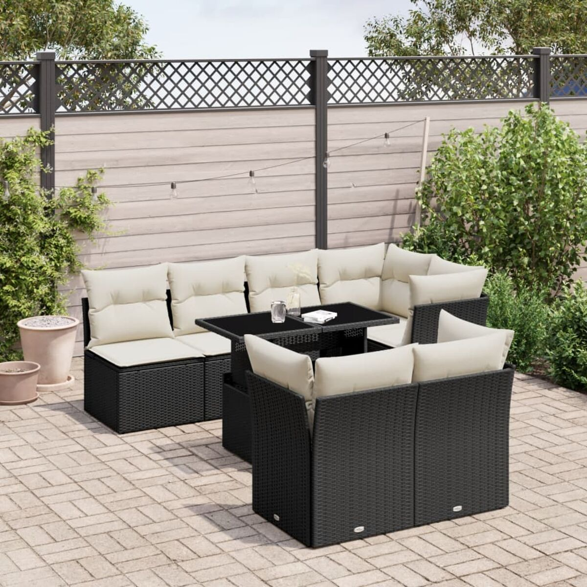 Schwarzes Rattan-Ecksofa mit cremefarbenen Kissen und einem Tisch mit schwarzer Glasplatte auf einer Terrasse.