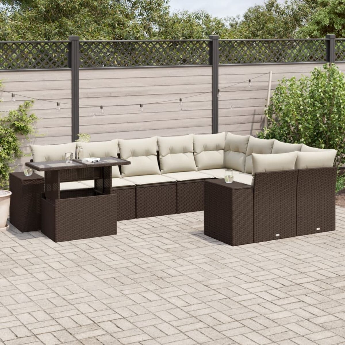 Outdoor-Ecksofa aus Korbgeflecht mit braunen Kissen und einem kleinen Tisch. Gepflasterte Terrasse und Zaun im Hintergrund.