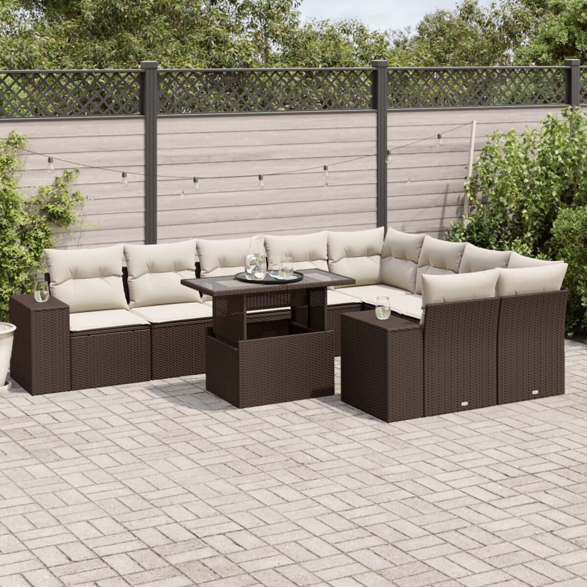 Set divani da esterno in vimini marrone con cuscini color crema e un tavolo nero.
