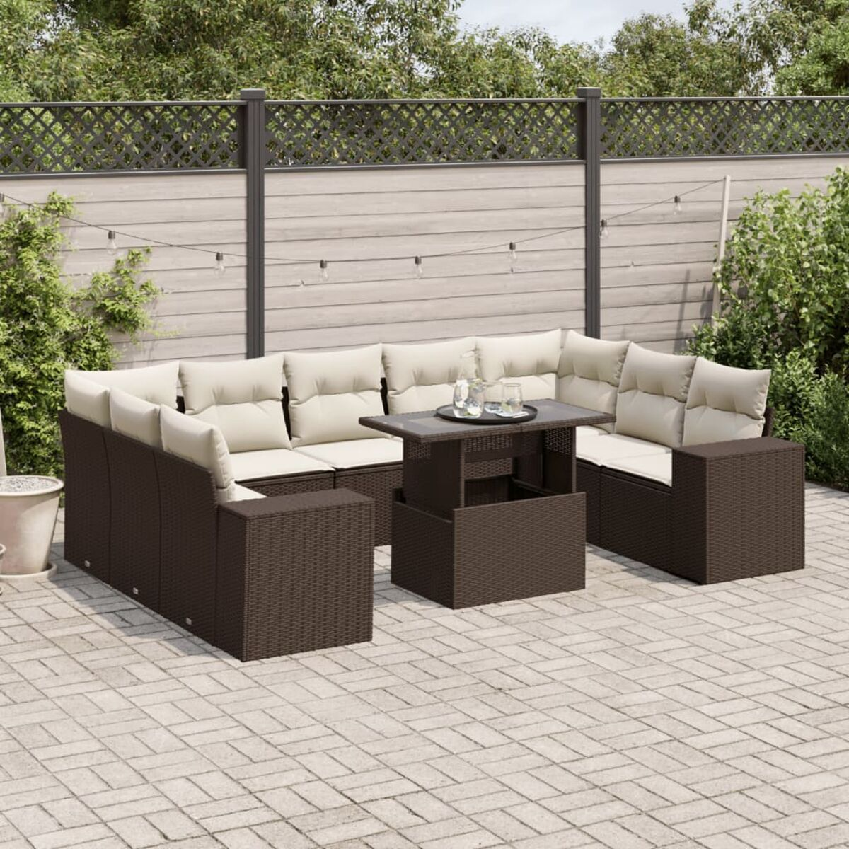 Set di sedute da esterno in rattan marrone. Cuscini beige. Tavolo con bevande. Patio grigio e luci.