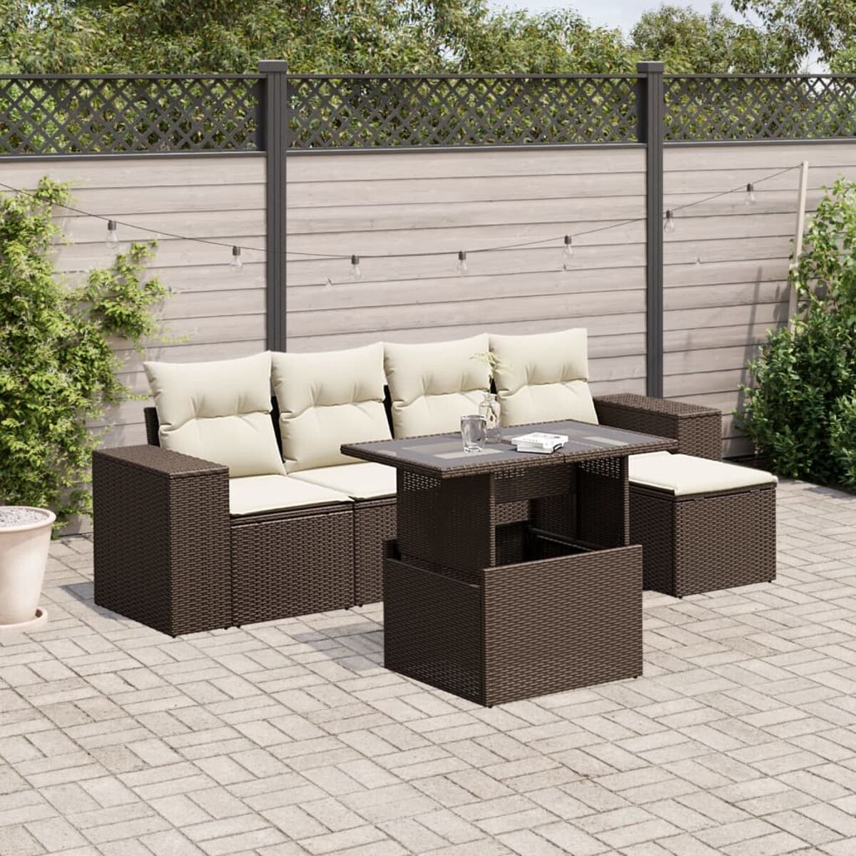 Set di sedute da esterno in vimini marrone scuro con cuscini color crema e tavolo elevabile. Sfondo è un patio.