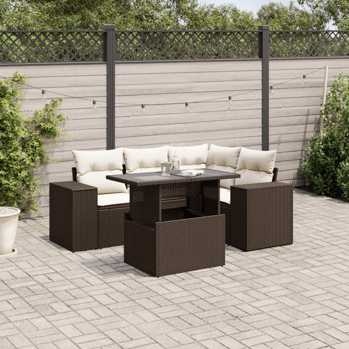 Set da esterno in vimini marrone scuro con tavolo e sedute. Ambientato su un patio in mattoni.
