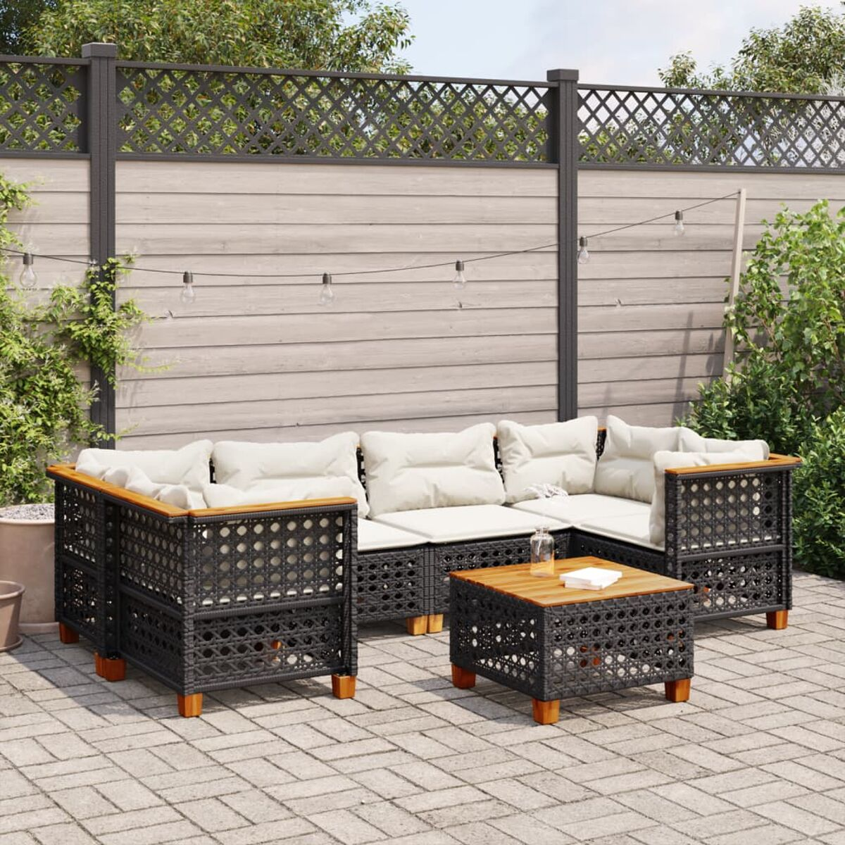 Gartenmöbel-Set. Es hat schwarze Korbsessel, einen Tisch und Lichterketten auf einer Terrasse.