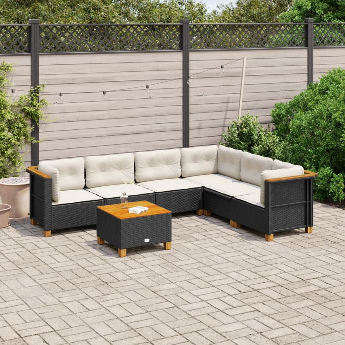 Schwarzes Rattan-Ecksofa mit beigen Kissen und einem Tisch. Hintergrund: Backstein-Patio, Zaun und Pflanzen.