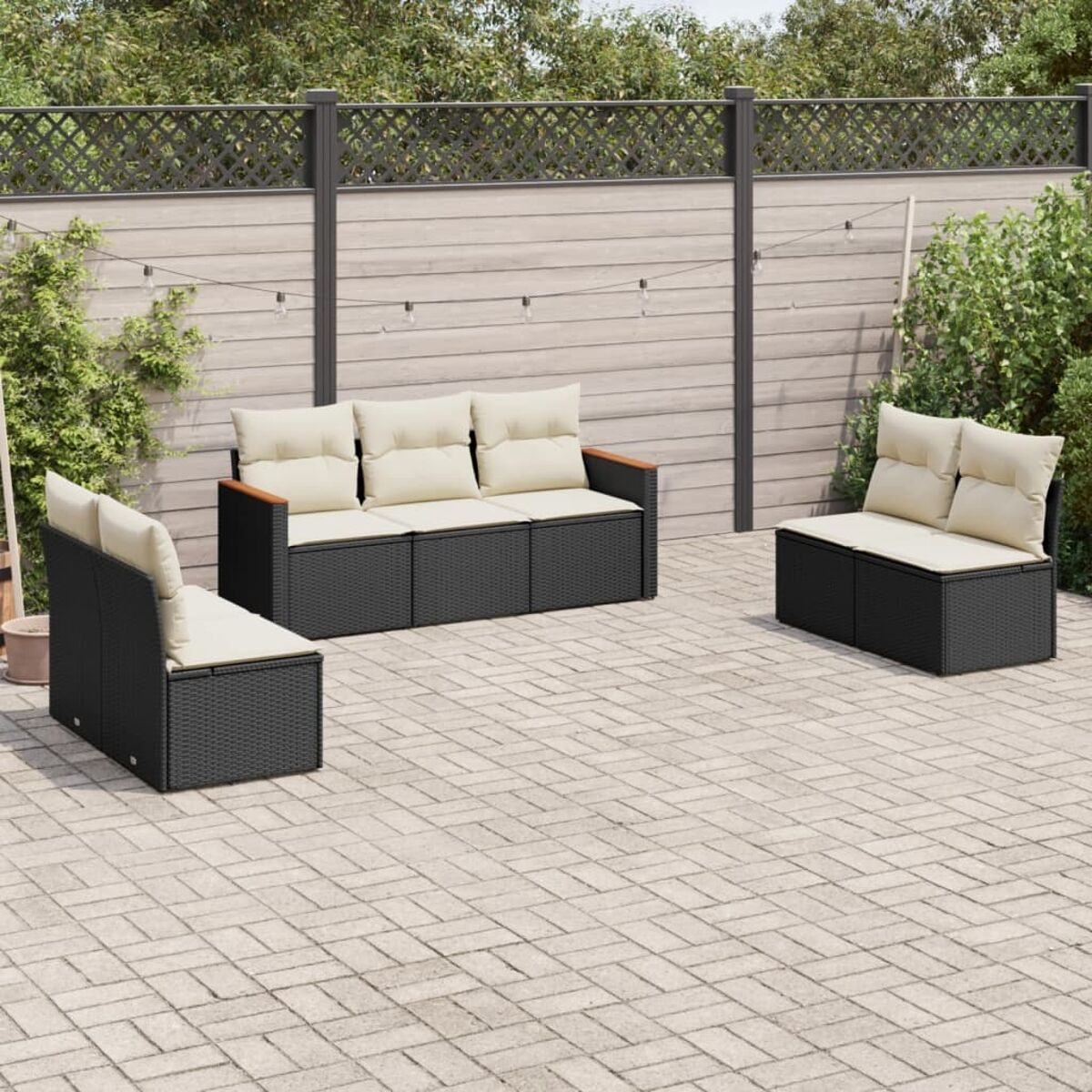 Rattan-Sofagarnitur mit beigefarbenen Kissen. Enthält ein 3-Sitzer-Sofa und zwei Sessel. Auf Ziegelterrasse.