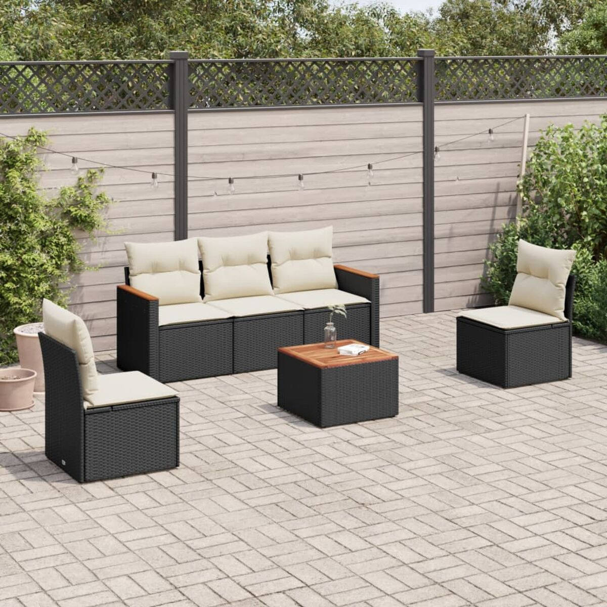 Schwarzes Outdoor-Set aus Korbgeflecht mit beigefarbenen Kissen und Holzakzenten auf einer Backsteinterrasse.