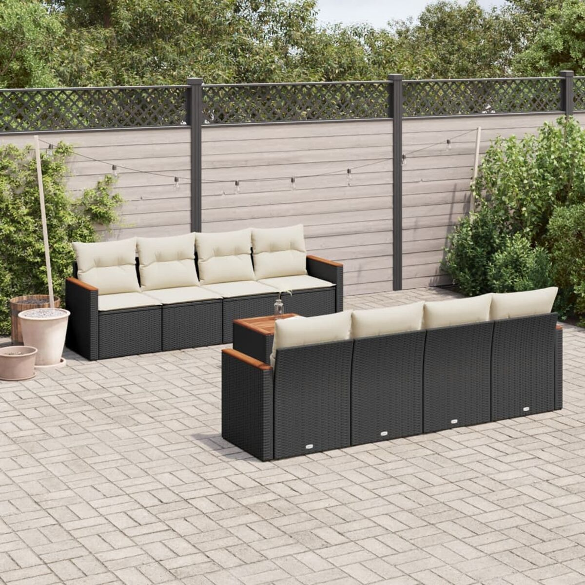 Zwei Korbsofa-Sets auf einer Ziegelterrasse, mit Zaun und dekorativen Lichtern im Hintergrund.