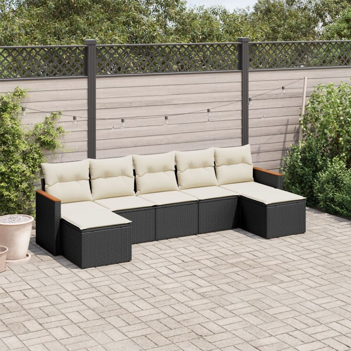 Schwarzes Rattan-Eck-Terrassenmöbel-Set. Beige Kissen, Holzakzente und ein Zaun mit Lichtern.