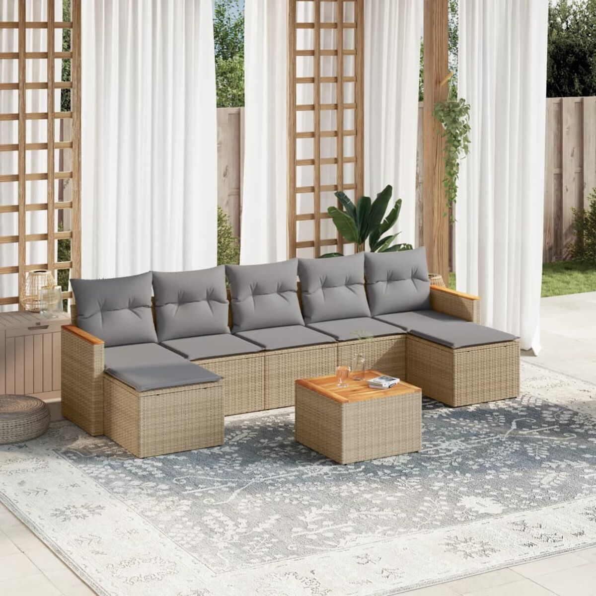 Beiges Outdoor-Möbelset aus Korbgeflecht mit grauen Kissen und einem Holztisch auf einem gemusterten Teppich.