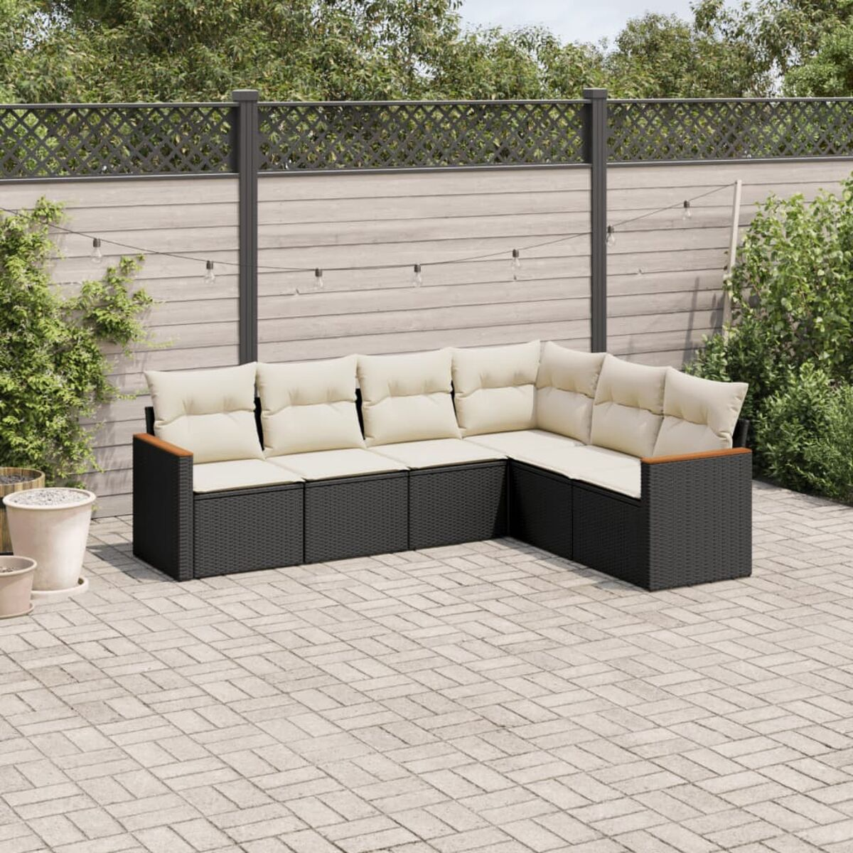 Schwarzes Rattan-Outdoor-Sofa mit cremefarbenen Kissen, auf einer Terrasse.