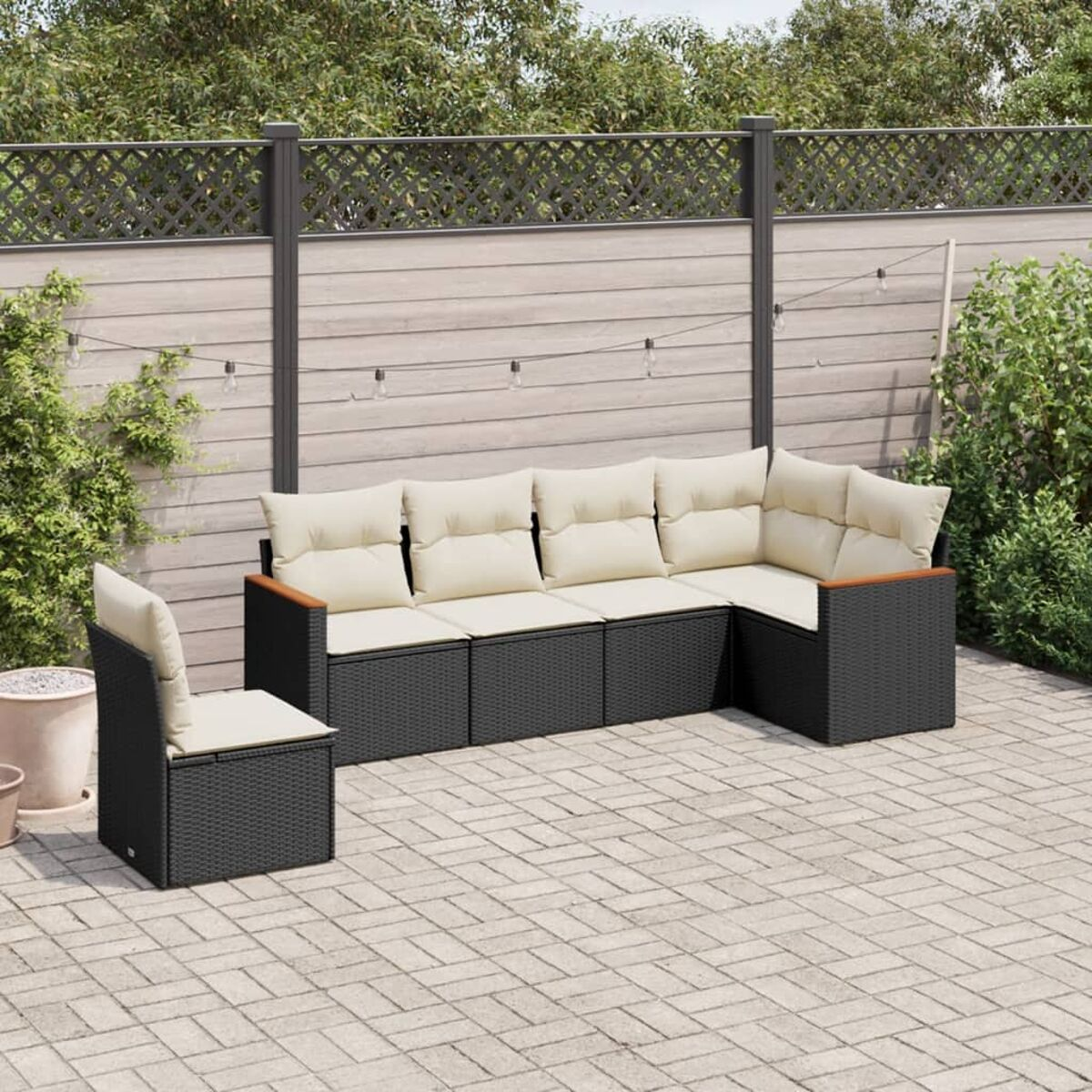 Ein braunes Rattan-Ecksofa mit beigen Kissen und einem Stuhl in einem Hinterhof.