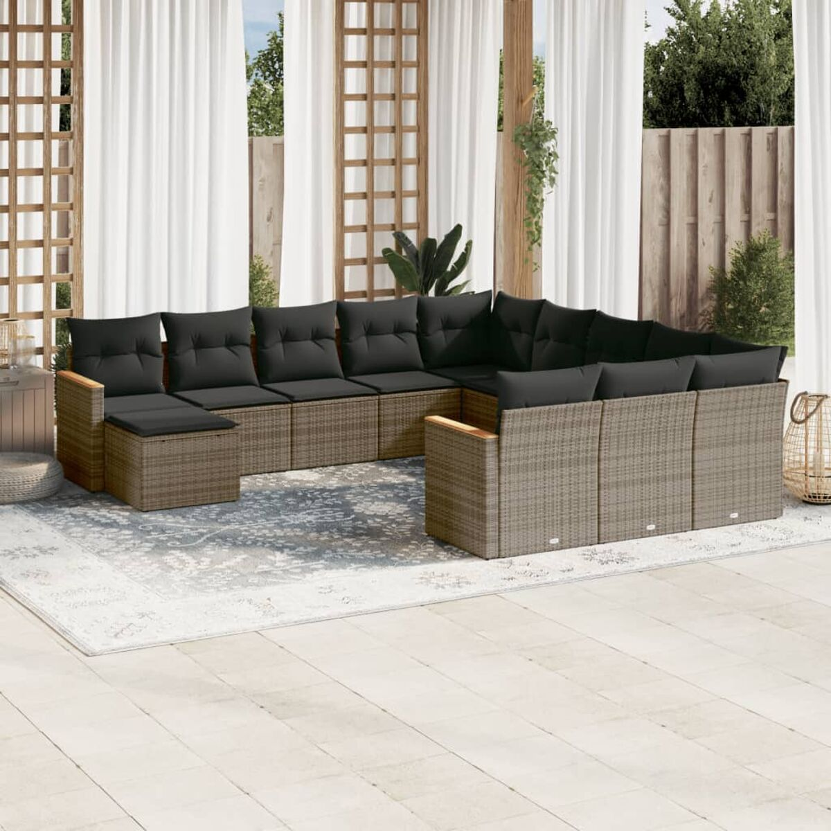 Rattan-Outdoor-Sofaset mit schwarzen Kissen auf einem weißen Teppich, Vorhängen und Holzzaun im Hintergrund.