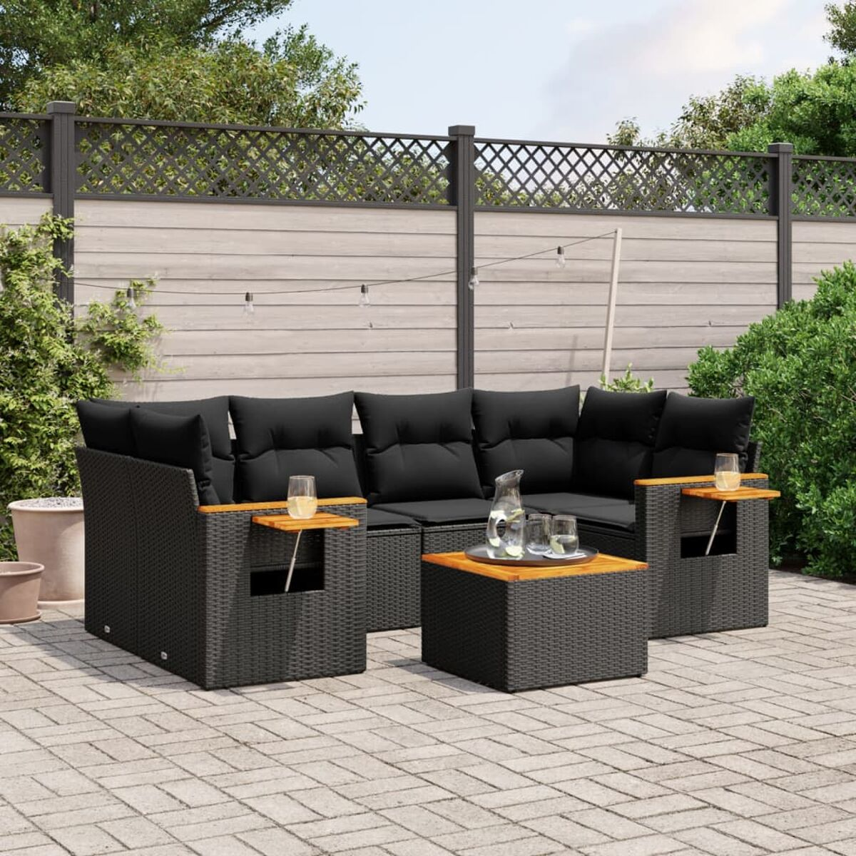 Outdoor-Sitzgruppe auf einer Ziegelterrasse. Schwarze Korbmöbel mit dunkelgrauen Kissen und Holztischen.